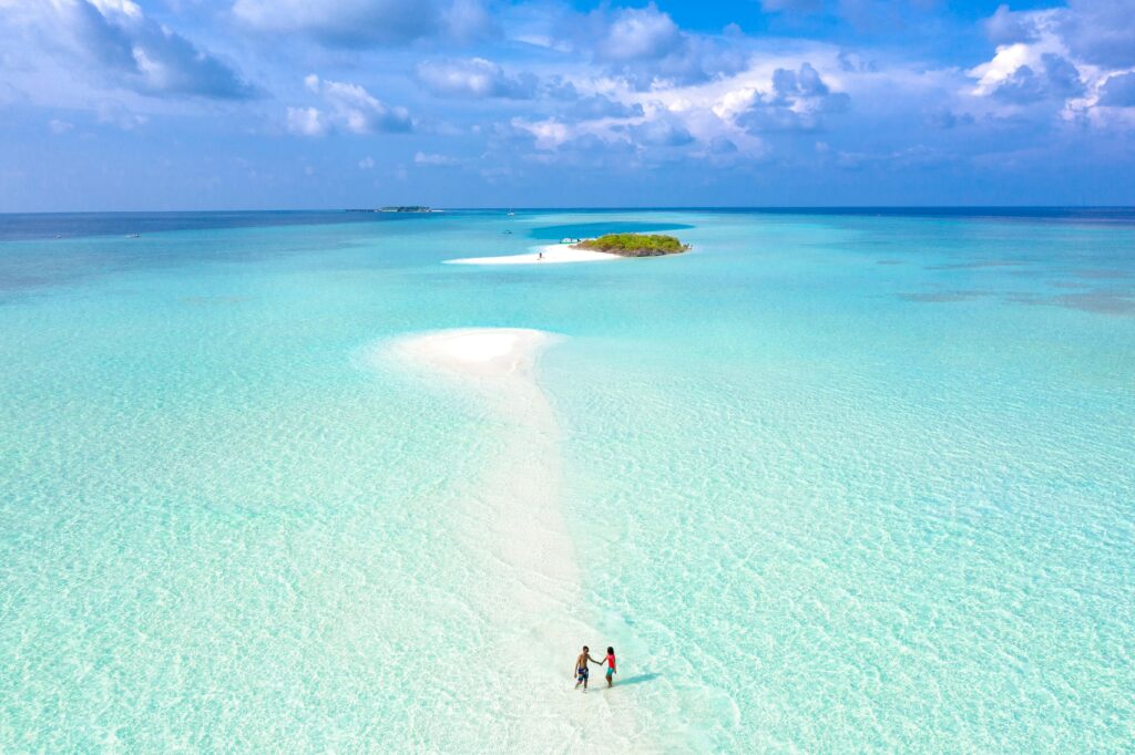 A couple holding hands on a picturesque sandbar surrounded by turquoise waters in a tropical paradise.